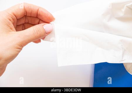 Female hand pulls white paper napkin from blue box on white background, care and beauty Stock Photo