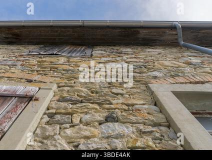 A low angle view of an old house facade built of massive stone with wooden shutters over the windows Stock Photo