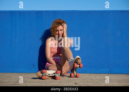 Young woman with roller skates posing against blue wall Stock Photo