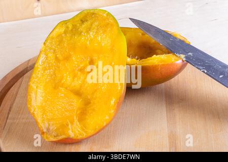 Side view of two halves of mango and kitchen knife on wooden background Stock Photo