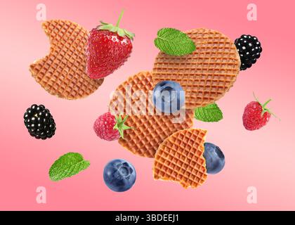 Tasty Dutch waffles, fresh berries and mint flying on pink gradient background Stock Photo