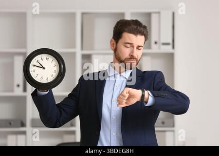 Stressed businessman looking at his watch and holding clock in office, Deadline concept Stock Photo
