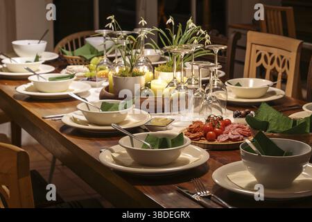 Dinner party for family and friends on a large wooden table with various vintage chairs, festive setting with crockery, wine glasses and decoration, d Stock Photo