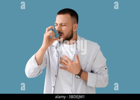 Young man with asthma attack using inhaler on blue background Stock Photo