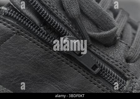A close-up macro shot of a black zipper on a black leather shoe, highlighting the texture of the material and the detail of the fastener. Stock Photo