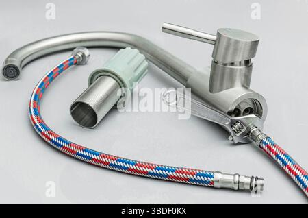 Close-up of a new stainless steel faucet, flexible water hoses, and an adjustable wrench, representing plumbing installation, home improvement, or rep Stock Photo