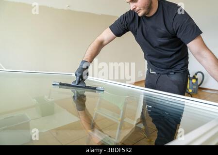 A professional cleaner using a squeegee and scraper to clean a large apartment window Stock Photo