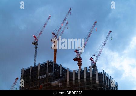 Looking up at five cranes on top of building that is being constructed against a cloudy night sky. Part of the Umekita redevelopment at Umeda, Osaka. Stock Photo