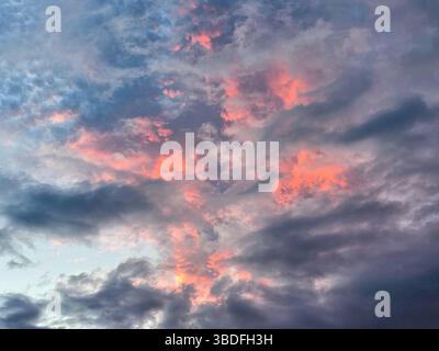 sunset colors the sky with shades of pink and orange, casting a warm glow across the textured layers of dark and light clouds Stock Photo