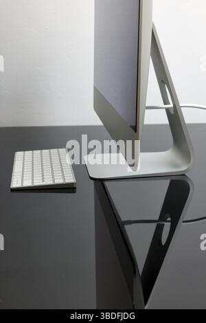 A modern desktop configuration showcases a stylish monitor resting on a sleek stand next to a compact keyboard. The glossy surface reflects the tech, Stock Photo