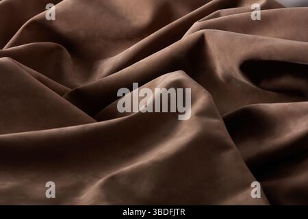 Rich brown fabric displays subtle waves and folds, capturing light beautifully in an indoor environment. The texture invites touch and evokes warmth a Stock Photo