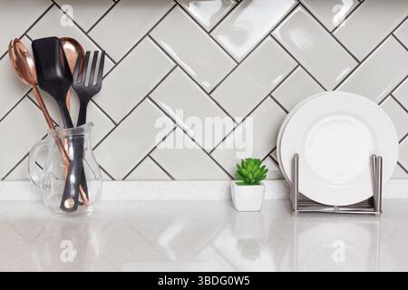 Kitchen utensils in glass jug and white dishes in dish rack rest on clean counter and glossy tile background, home decor, kitchen styling Stock Photo