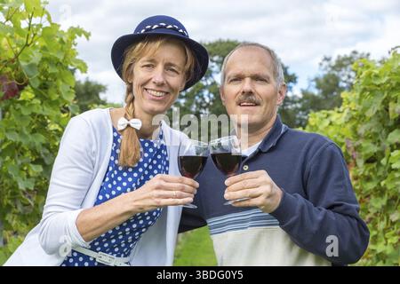 Caucasian middle aged couple toasting with glasses of red wine in vineyard Stock Photo