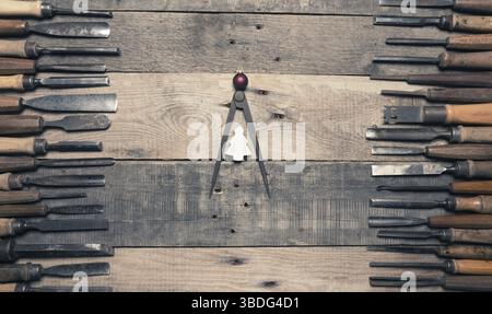Many firmer chisels as frame on a rustic workbench, a steel compass as Christmas tree in the middle! Construction holidays background Stock Photo