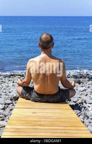 Middle aged man meditating at coast and ocean Stock Photo