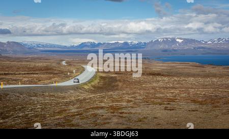 Winding tarmac road 36 with cars driving along Thingvallavatn lake in Thingvellir National Park, Iceland, lava fields and snowcapped mountains. Stock Photo