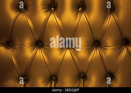 The texture of the leather sofa upholstery in gold color, with rivets. Stock Photo