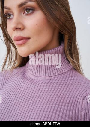 Woman with long hair wearing a ribbed purple turtleneck sweater gazes slightly upward. The close-up captures her serene expression and subtle makeup Stock Photo