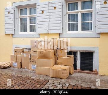 Freiburg, Germany - Feb 10, 2025: Stack of cardboard boxes labeled Tamaris placed outside a pastel yellow building with cobblestone pavement and shutt Stock Photo