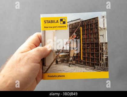 Paris, France - Mar 10, 2025: Hand holding a STABILA catalog featuring a construction worker using a measuring level tool on a building site, with bra Stock Photo