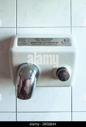 Lyon, France - Oct 4, 2023: Wall-mounted vintage hand dryer with chrome nozzle and push button, labeled in German, fixed on white tiled restroom wall Stock Photo