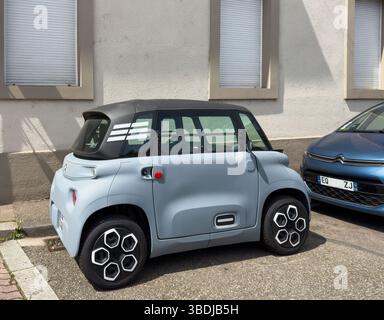 Paris, France - Jun 9, 2024: A compact Citroen Ami electric vehicle is parked on a sunny street beside a building with shuttered windows, showcasing i Stock Photo
