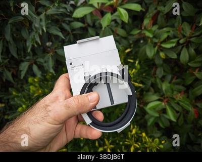 Paris, France - Feb 26, 2024: A hand holds an Apple Thunderbolt 4 Pro Cable box in front of lush green foliage outdoors, with the coiled black braided Stock Photo