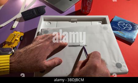 Paris, France - Apr 9, 2025: Hands performing a pencil rubbing over embossed MacBook Air M4 text on packaging paper, surrounded by a LEGO taxi, retro Stock Photo
