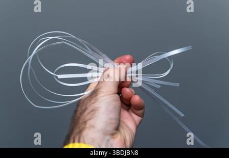 A close-up view of a hand tightly gripping several translucent white cable ties with looped ends against a plain neutral grey background in a well-lit Stock Photo