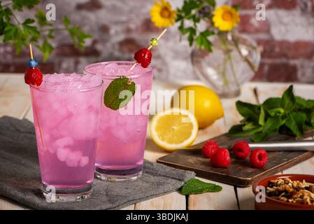 Glasses of ice with lemon and raspberry soda made from fruit juice, next to a cutting board with raspberries and lemons. Stock Photo
