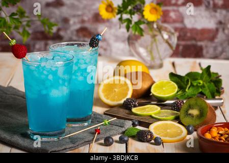 Glasses of ice and a blue exotic fruit soda, made from fruit juice, next to a cutting board with pieces of various exotic fruits. Close-up. Stock Photo