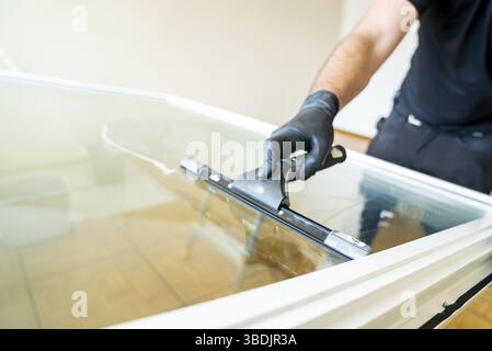 A professional cleaner using a squeegee and scraper to clean a large apartment window Stock Photo