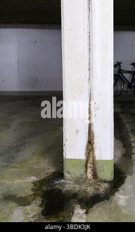 water damage in concrete construction with calcium and rust deposits and puddles near a supporting wall pillar in a garage Stock Photo