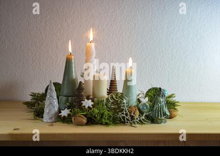 Third Advent, decoration with four different candles, three are lit, some moss, green Christmas balls from glass and cinnamon stars on a wooden board Stock Photo