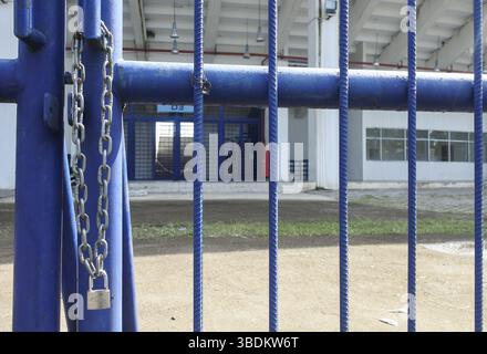iron chain and padlock key, hanging on a blue iron fence door in front of a building. Stock Photo
