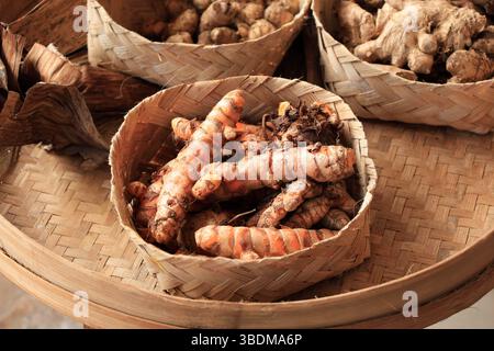 Fresh Kunyit or Turmeric Root on Besek or Bamboo Weaving Box Basket, CLose Up with Ginger Root on Background Stock Photo