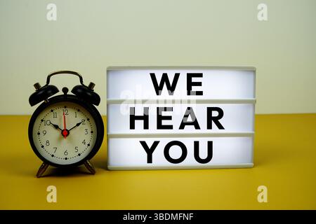 We Hear You text on LED lightbox with alarm clock on yellow background Stock Photo
