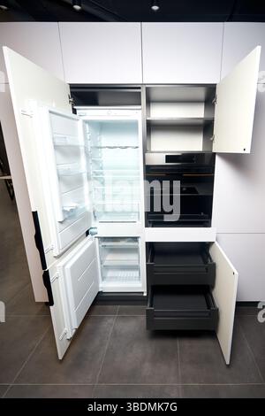 Vertical shot of kitchen interior with beige wooden furniture and modern appliances. Opened built integrated refrigerator with opened door empty shelv Stock Photo