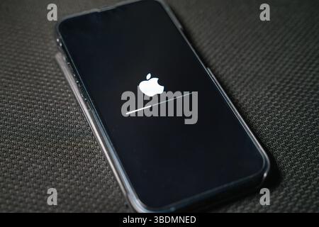 iPhone displays the iconic white Apple logo against a black background during the boot-up and upadate process, resting on a textured dark surface. Stock Photo