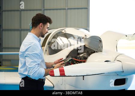 Aircraft mechanic using digital tablet performing maintenance check on small airplane engine Stock Photo