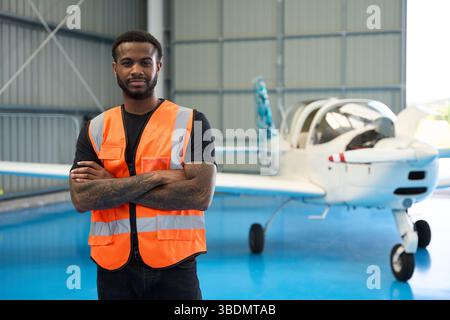 Aircraft mechanic posing with arms crossed in hangar with small airplane Stock Photo