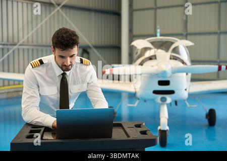 Pilot using laptop in hangar with small airplane Stock Photo