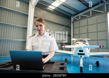 Female pilot using laptop in aircraft hangar with small plane Stock Photo