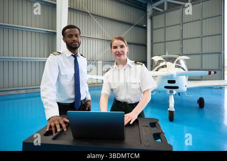 Aircraft maintenance training: pilots using laptop in hangar with small airplane Stock Photo