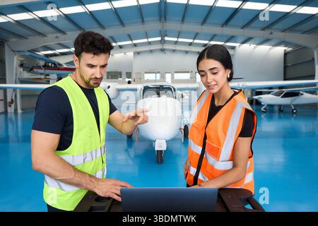 Aircraft mechanics using laptop, discussing maintenance in hangar Stock Photo