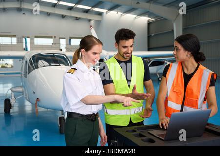 Pilot and mechanics discussing maintenance using laptop in hangar Stock Photo