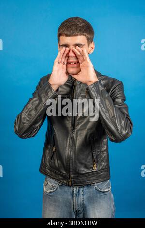 Studio shot of a young man wearing casual clothes and shouting with hands cupped around his mouth Stock Photo