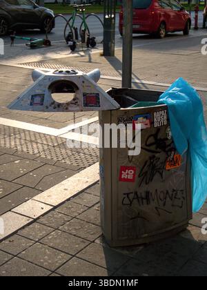 Urban Trash Bin with Graffiti and Blue Plastic Bag on a Cityside Walkway Stock Photo