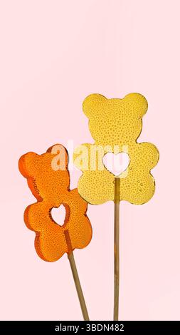 Sweet love. Vertical banner for Valentine's Day. Two transparent lollipops in the shape of bears with a heart on a pink background. Stock Photo