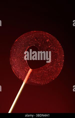 Love. A round transparent red lollipop on a dark red background. Vertical banner for Valentine's Day. Stock Photo